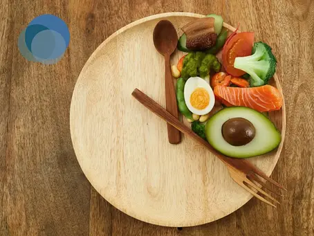 Foto de qualidade de um prato com os talheres e alimentos saudáveis simbolizando um relógio marcando 8 horas, que é a janela de alimentação abordada no texto sobre jejum intermitente