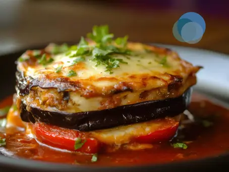 Foto mostra um dos itens do cardápio low carb: prato de lasanha de berinjela em close-up, destacando a textura do molho, queijo derretido e pedaços de berinjela e tomate.