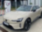 Beige Volvo ES90 EV charging at a public station, with German plate, tiled forecourt, and modern industrial building in back.