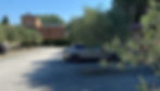 Gravel courtyard with parked Volvo ES90 beside brick buildings and olive trees under a clear blue sky.