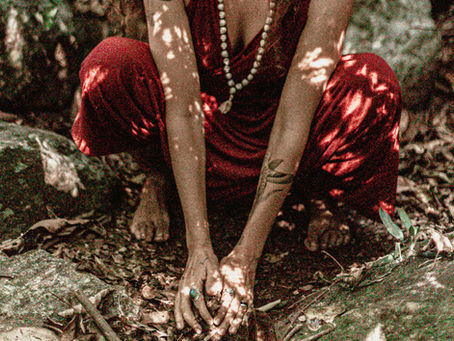 Uma mulher de cócoras, agachada, colocando as mãos na terra