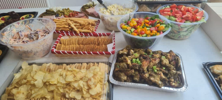 A buffet table filled with various dishes, including a colorful salad, grilled chicken, crackers, chips, and creamy coleslaw, creating a festive and inviting setting