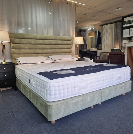 Luxurious bedroom featuring a plush bed with an olive green upholstered headboard, flanked by elegant lamps on dark nightstands, exuding comfort