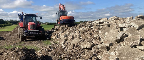 A red tractor and an orange excavator are parked on a construction site beside a large pile of rubble