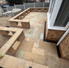 A newly built raised deck made of light gray composite panels with dark posts, three steps, and landscaped surroundings of paving stones and gravel, in a residential backyard