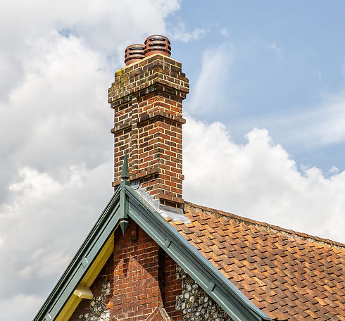 Traditional weathered brick chimney stack with leadwork detailing on a residential roof peak