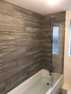 Built in bathtub shower unit with large grey wood grain effect ceramic wall tiling