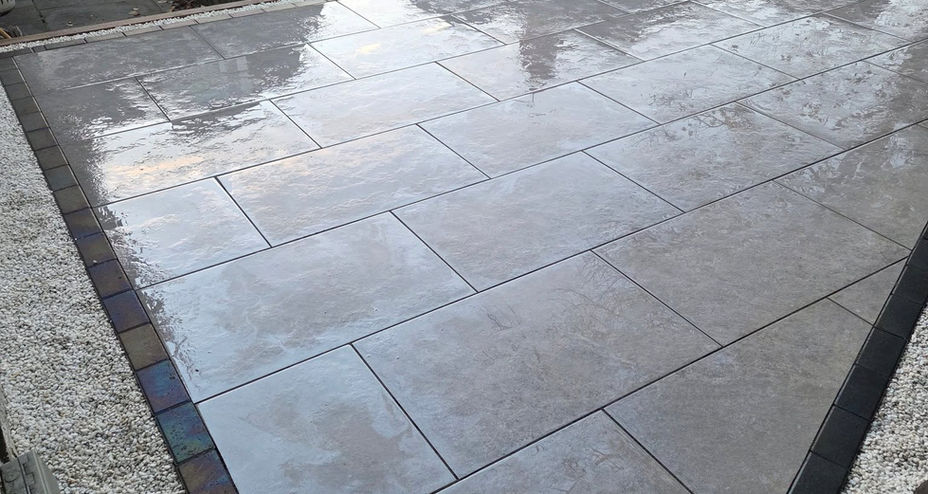 Clean stone patio flags with dark grey block paving borders reflecting light after being washed