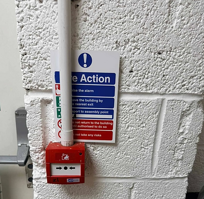 Red manual fire alarm call point box mounted on a white brick wall