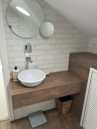 Small bathroom corner featuring a circular mirror, wall-mounted chrome faucet, and white vessel sink on wooden vanity