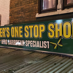 Large printed banner sign for "TEX'S ONE STOP SHOP" mounted on a brick wall.