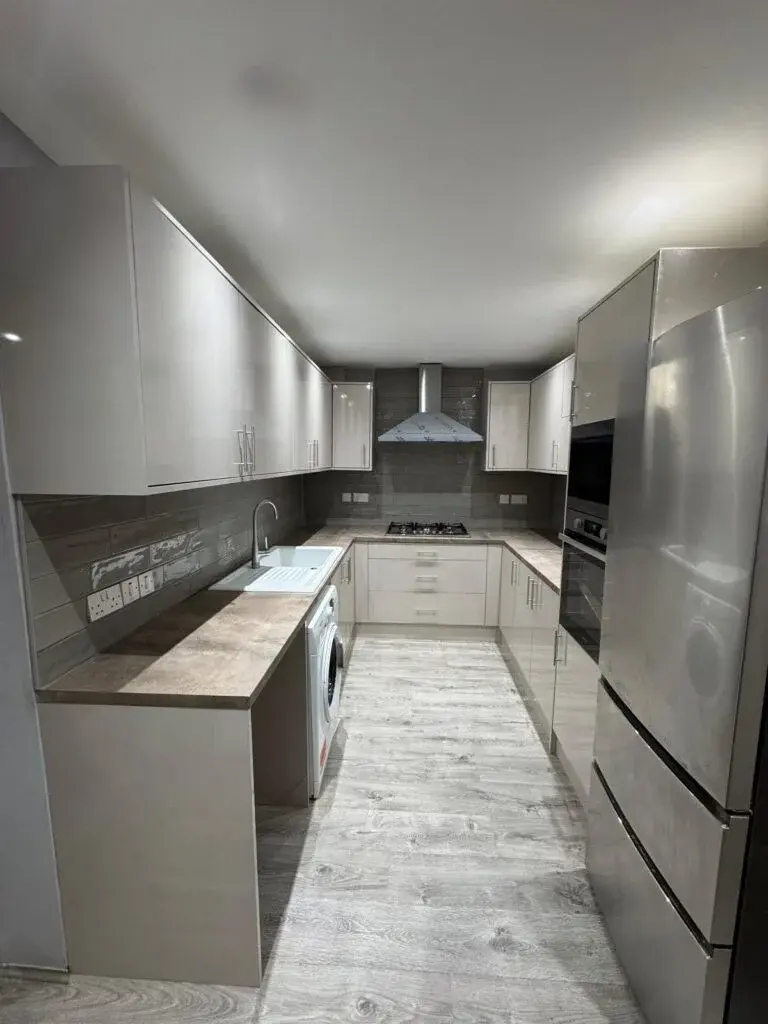 Modern U-shaped kitchen with white gloss cabinets, grey tile backsplash, and stainless steel appliances