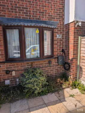 EV charger in black mounted on a residential red brick house wall next to a garden bush