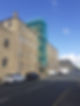 Street view of a historic brick building with green scaffolding on one side under clear blue skies