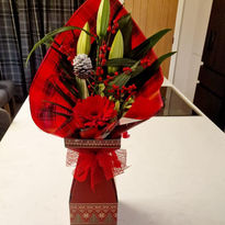 A vibrant holiday arrangement with red gerberas, green lilies, and winter berries wrapped in bold red paper
