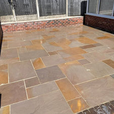 A rectangular raised platform of gray composite decking with black trim, set on a green lawn against a white fence decorated with butterfly ornaments and climbing plants