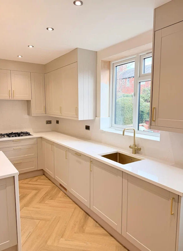 Modern fitted kitchen with taupe cabinetry, white quartz worktops, and gold hardware