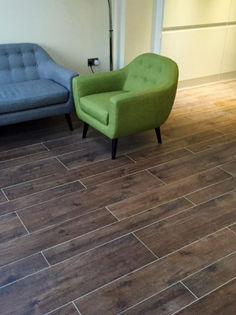 Open plan living area featuring dark wood effect floor tiling with a sofa and green armchair