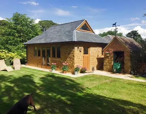Stone outbuilding extension with slate roof in a sunny landscaped garden