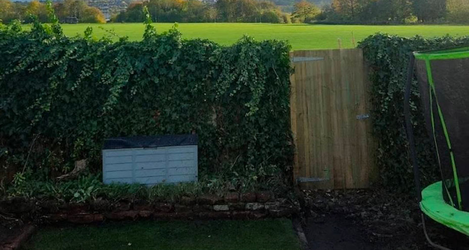 Small green lawn in a rectangular garden overlooking open countryside fields beyond the fence