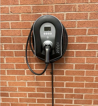 Wall-mounted electric vehicle charger on a brick wall, featuring a coiled cable and digital display