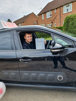 A person in a black car holds a certificate through the open window, smiling.