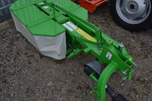 A green agricultural machine with a beige cover, set on a gravel surface