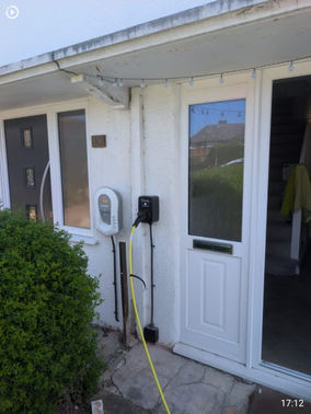 Electric car charger with tethered cable installed on a white rendered house wall