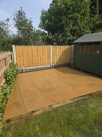 Smooth beige patio flags laid next to a newly installed wooden fence with concrete posts and a garden shed