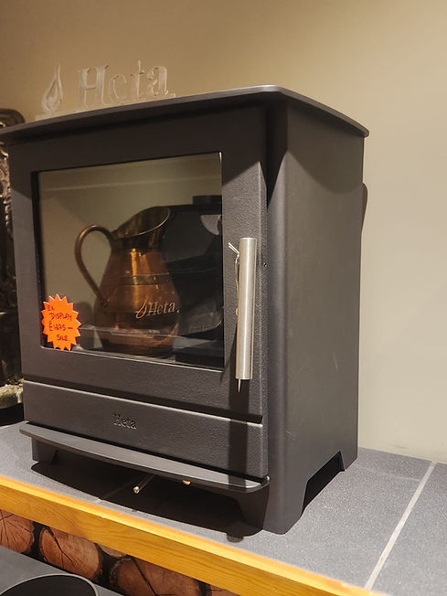 alt text: "A black Heta wood-burning stove with a glass front, displaying a copper pitcher inside
