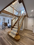 Carpeted staircase with oak handrails and glass balustrades in a modern home hallway