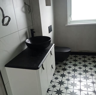Monochromatic bathroom featuring a white vanity with a black vessel sink and patterned black-and-white floor tiles.