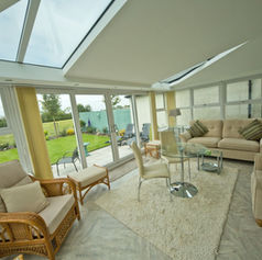 Contemporary home extension with bi-fold glass doors opening to garden, furnished with sofas, coffee table, TV, and kitchen area