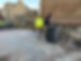 Two people cleaning an alley next to a stone wall
