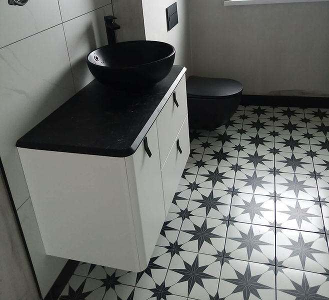 Modern bathroom with a black vessel sink on a white cabinet, black toilet, and patterned black and white star tiles