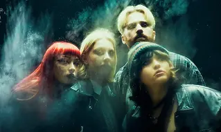 Four people stand closely together in a smoky, ethereal atmosphere.