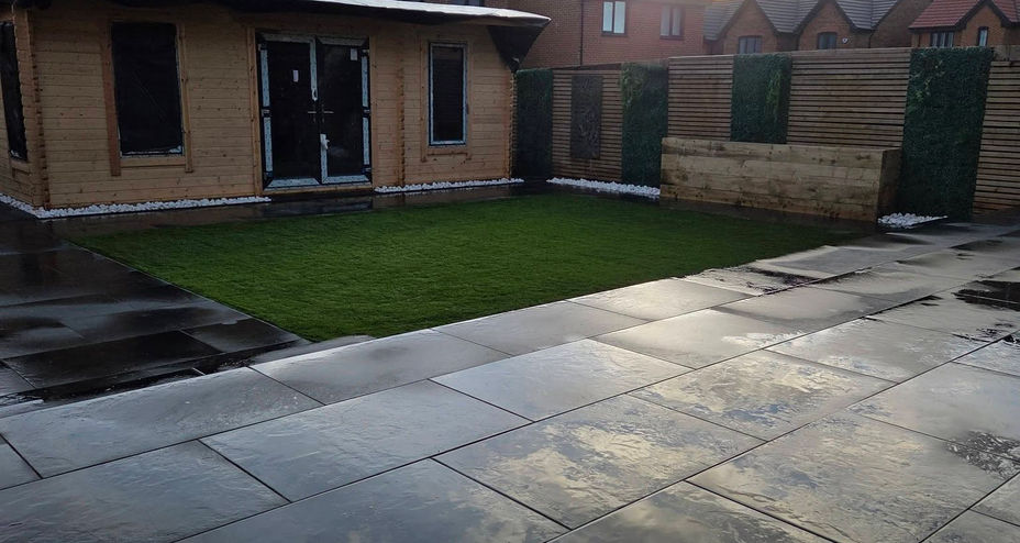 Modern garden layout showing artificial turf surrounded by dark grey patio paving flags