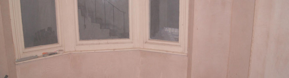 Empty room with bare plaster walls, beige flooring, and a curved bay window
