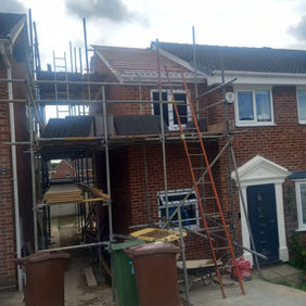 Rear view of a house extension project with metal scaffolding and building materials on a construction site