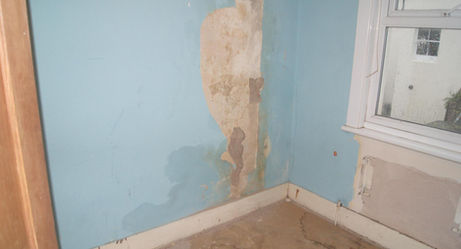 A room with peeling blue paint, water-damaged walls, and visible damp patches