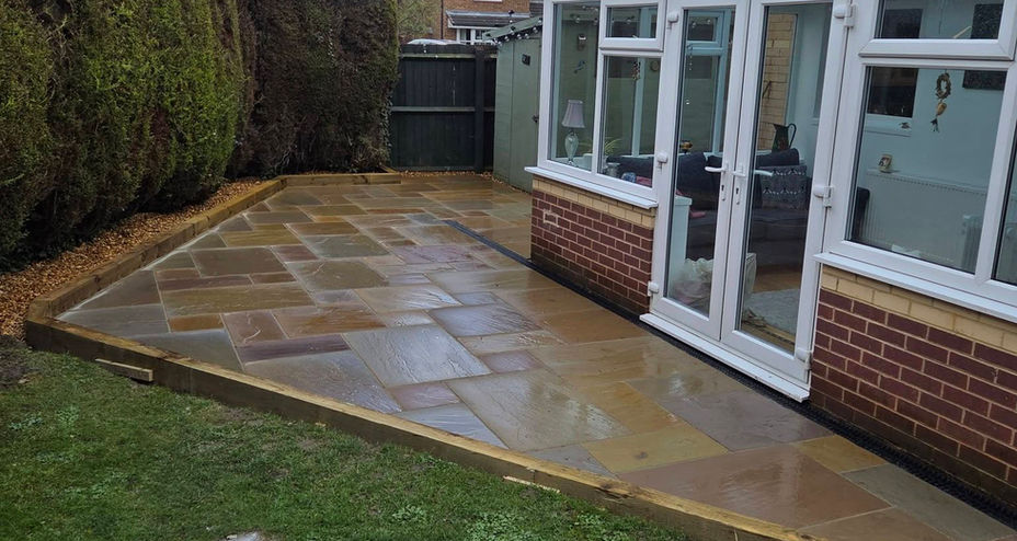 Curved garden patio area laid with light grey stone flags next to a white conservatory