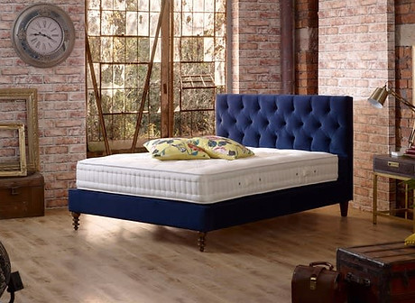 Blue tufted fabric bed frame with a mattress in a modern brick wall bedroom