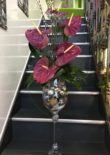 Large magenta anthuriums in a tall glass vase on stairs