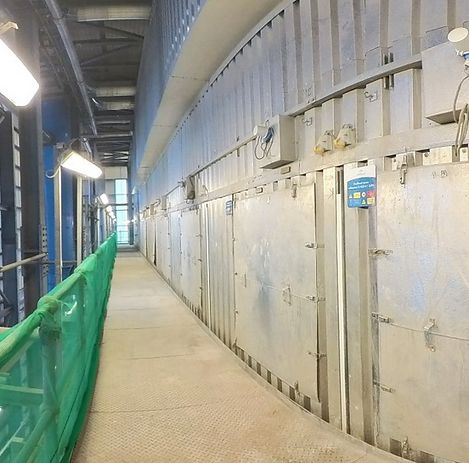 A narrow industrial corridor with metal walls and a green safety net on the left