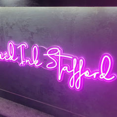 Vibrant pink neon sign spelling out cursive text on a dark interior wall.