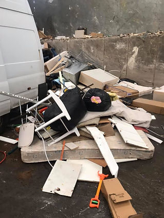 A pile of construction debris, including wood and insulation, is scattered outside a weathered stone building with red doors