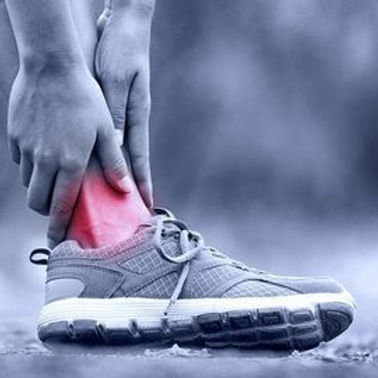 Person holds their red, painful ankle above a gray running shoe, indicating an injury