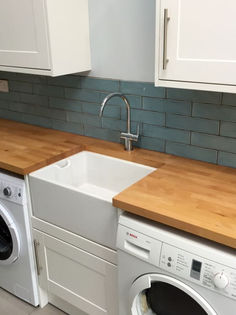 Utility room with white washing machines wooden worktops and teal metro tiled splashback