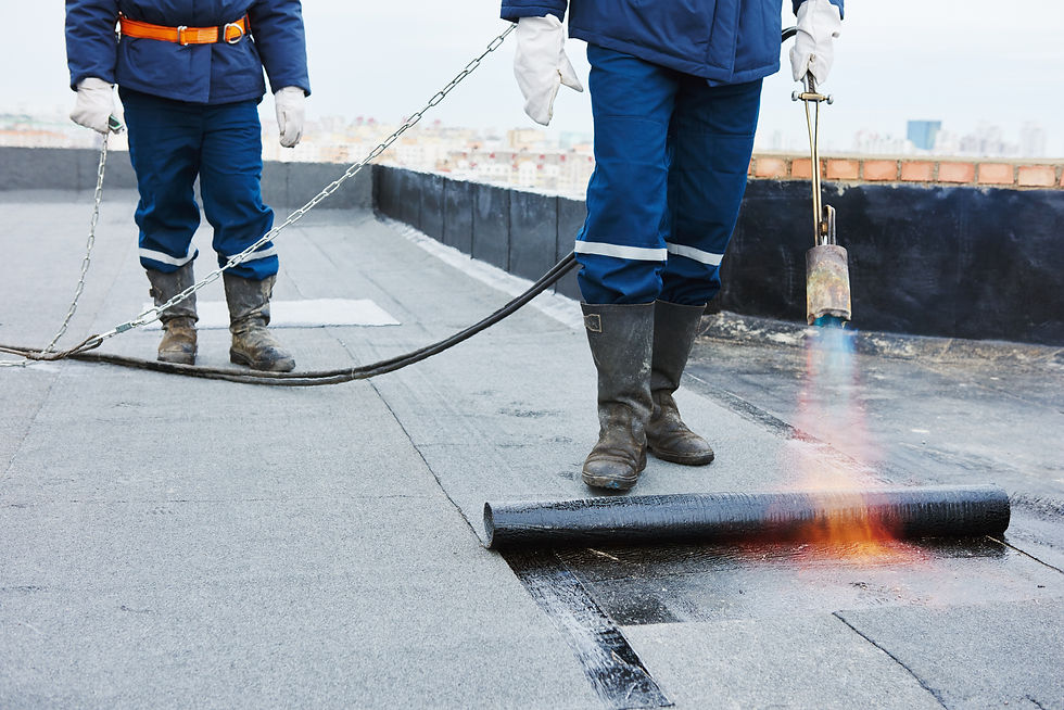 Worker using a gas blowtorch flame to melt and seal a roll of bitumen waterproofing onto a flat roof