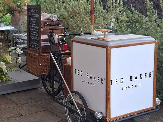 A white mobile ice cream cart attached to a bicycle parked outdoors next to a brick path